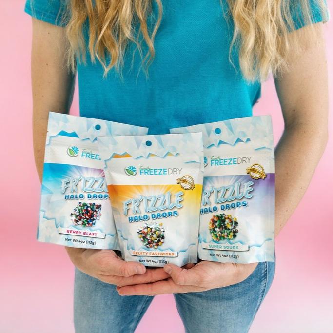 Group picture of our freeze dried Halo Drops being held by a person in blue with a pink background